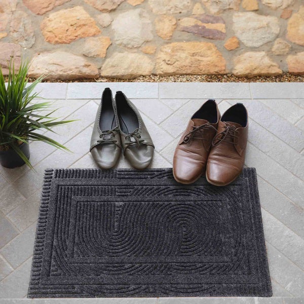 Fußmatte mit Muster, zwei Paar Schuhe und Topfpflanze vor einer Wand