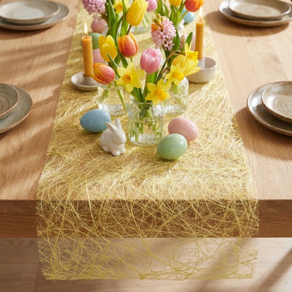 Festlich gedeckter Holztisch mit frühlingshafter Dekoration aus Blumenvasen, Ostereiern und einem filigranen Tischläufer in Netzoptik.