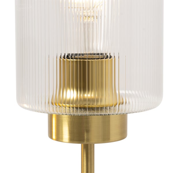 Nahaufnahme einer Lampe mit geriffeltem Glasschirm und goldenem Sockel.
