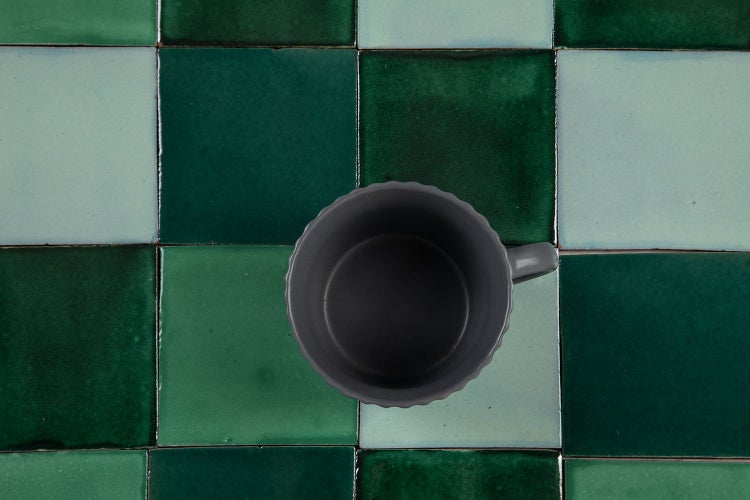 Graue Tasse auf grünem Fliesenhintergrund