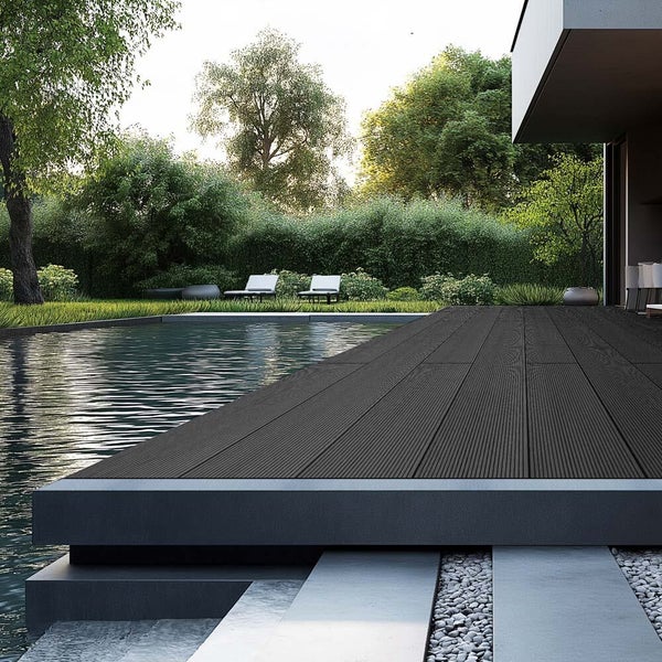 Moderne Terrasse mit dunklen, strukturierten Terrassendielen neben einem Pool, umgeben von einem grünen Garten mit Bäumen und Sonnenliegen.