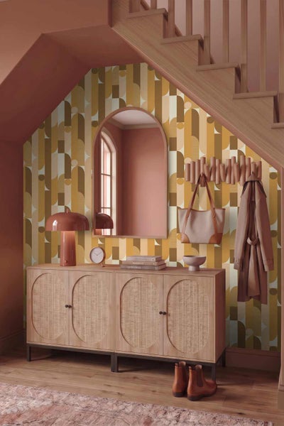 Moderner Flur unter einer Treppe mit geometrisch gemusterter Tapete, Sideboard aus Holz mit Rattantüren, Pilzleuchte, Spiegel und Garderobe.