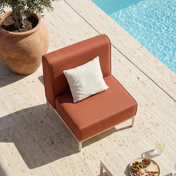 Moderner Garten-Lounge-Sessel mit terracottafarbenem Polster und weißem Kissen an einem Pool auf einer hellen Steinterrasse.