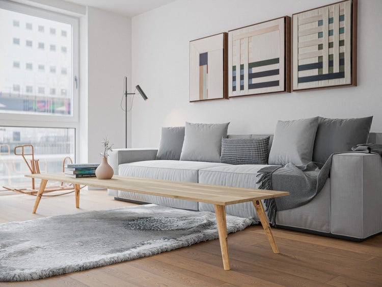 Modernes helles Wohnzimmer mit grauem Modulsofa aus Stoff, langem Couchtisch aus Holz und grauem Hochflor-Teppich auf Parkettboden.