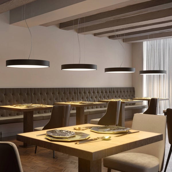 Vier runde schwarze LED-Pendelleuchten hängen über Tischen in einem modernen Restaurant mit Holzbalkendecke und eleganter Bestuhlung.