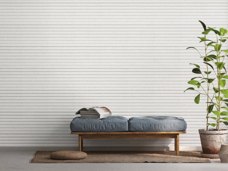 Holzbank mit zwei Sitzkissen, Buch und Topfpflanze vor einer strukturierten Wand in einem hellen, modern eingerichteten Raum.