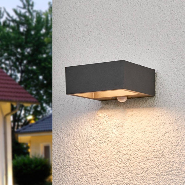 Moderne rechteckige Außenwandleuchte mit Bewegungsmelder an einer Hauswand, Lichtstrahl nach unten gerichtet.