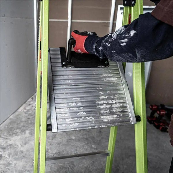 Hand mit Arbeitshandschuh hält eine Metallplattform an einer Trittleiter.