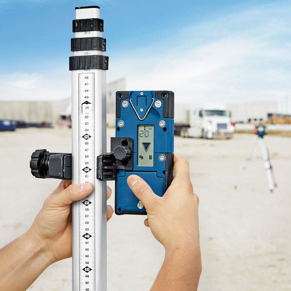 Hände justieren ein digitales Nivelliergerät an einer Messlatte für präzise Messungen.