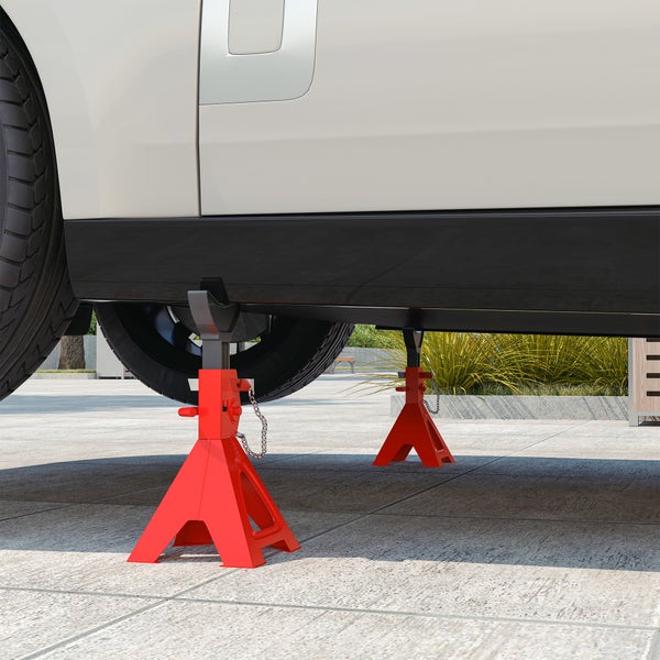 Zwei rote Unterstellböcke aus Metall stützen ein weißes Fahrzeug auf einer gepflasterten Fläche.