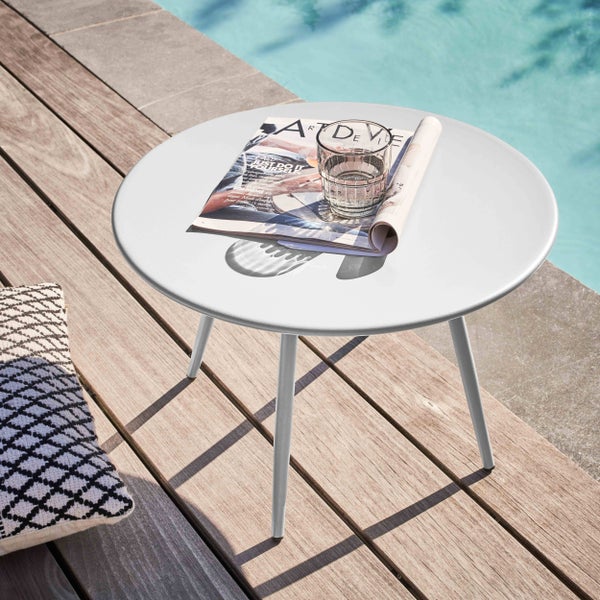 Runder Beistelltisch aus Metall auf einer Holzterrasse am Pool mit Magazin und Wasserglas.