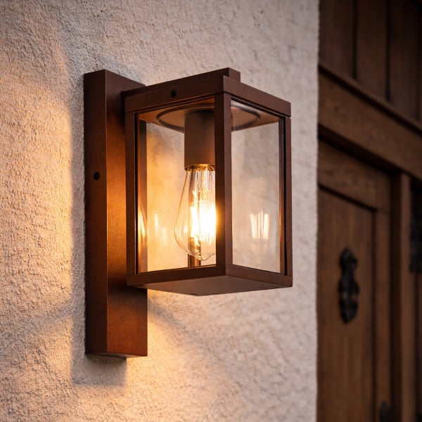 Rechteckige Außenwandleuchte aus Metall und Glas mit eingeschaltetem Leuchtmittel im Vintage-Stil an einer Hauswand.