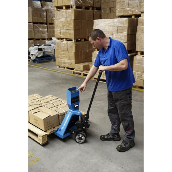 Ein Mann in einem Lager bedient einen blauen Hubwagen mit integrierter Waage, um eine beladene Holzpalette zu transportieren.