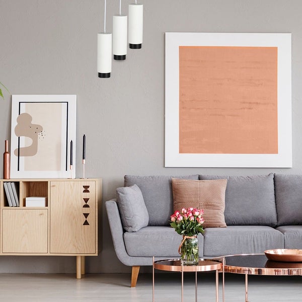 Modernes Wohnzimmer mit grauem Sofa, Holz-Sideboard, drei zylindrischen Pendelleuchten und kupferfarbenen Couchtischen.