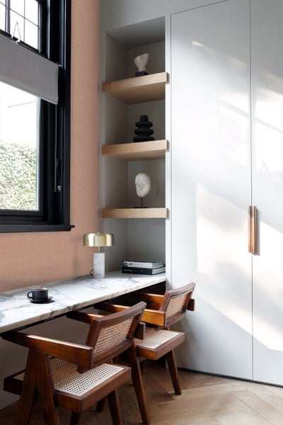Modernes Arbeitszimmer mit pfirsichfarbener Strukturtapete, Marmortisch, Holzstühlen und Einbauregalen neben einem weißen Schrank.