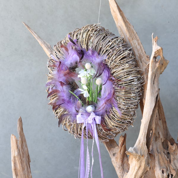 Dekorativer Kranz aus Zweigen mit Federn, Blumen und Schleife