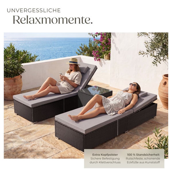 Zwei Gartenliegen aus Polyrattan mit grauen Auflagen und Kopfpolstern sowie ein Beistelltisch auf einer Terrasse mit Meerblick.
