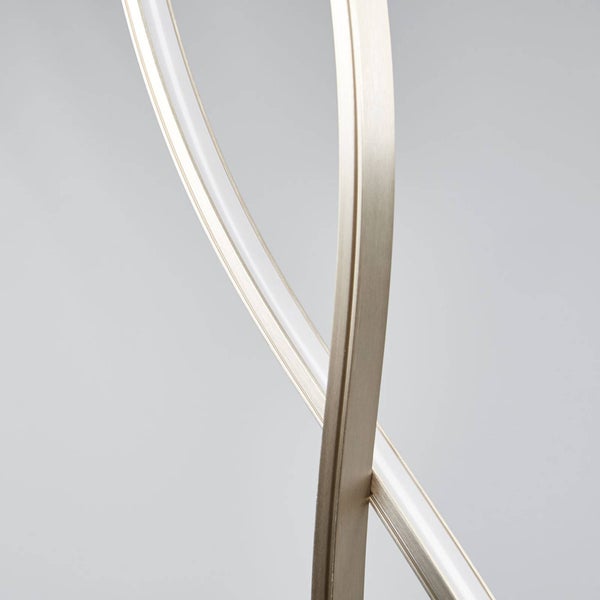 Detail einer modernen LED-Leuchte mit gekreuzten, geschwungenen Bändern aus gebürstetem Metall und integriertem Leuchtmittel.