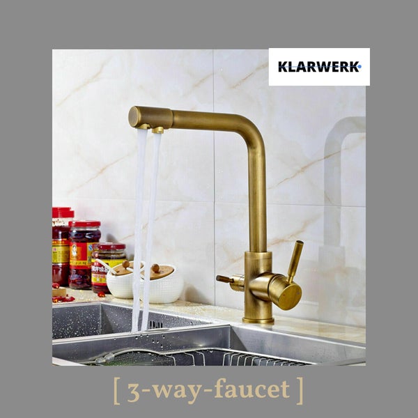 3-Wege-Küchenarmatur in Messing-Optik mit zwei Ausläufen an einer Edelstahlspüle vor einer hellen Fliesenwand und Klarwerk Logo.