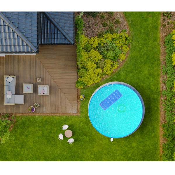 Vogelperspektive eines Gartens mit rundem Aufstellpool, einer Holzterrasse mit Lounge-Möbeln, gepflegtem Rasen und bepflanzten Beeten.