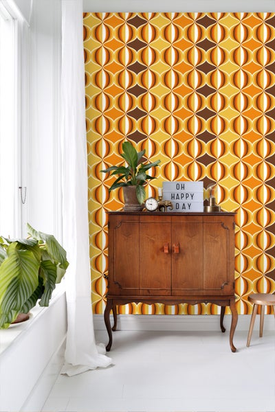 Raum mit Retro-Tapete in Braun, Gelb und Orange, Holzkommode, Pflanze und Dekoration.