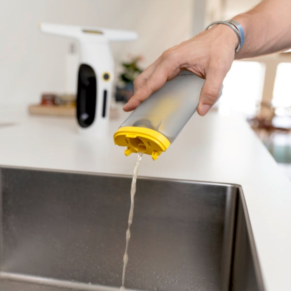 Person entleert den Wassertank eines Akku Fenstersaugers über einer Küchenspüle