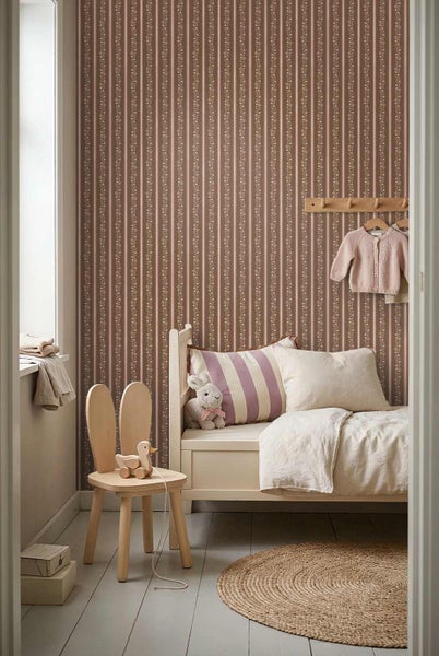 Kinderzimmer mit gestreifter Blumentapete, einem Bett aus Holz, einem Stuhl mit Hasenohren und einem runden Teppich aus Jute.
