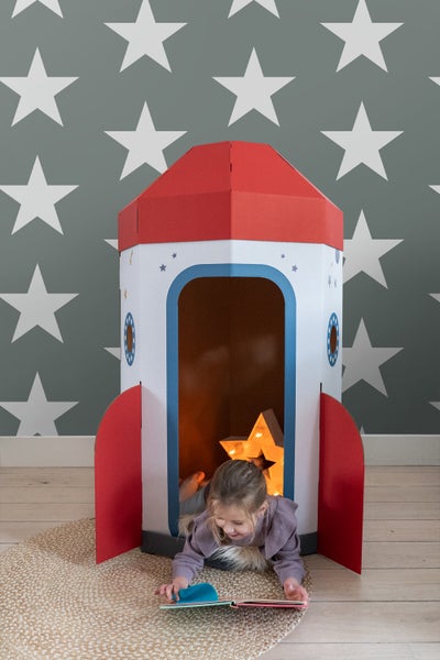 Mädchen liest Buch vor Papprakete mit Sternenlicht im Kinderzimmer