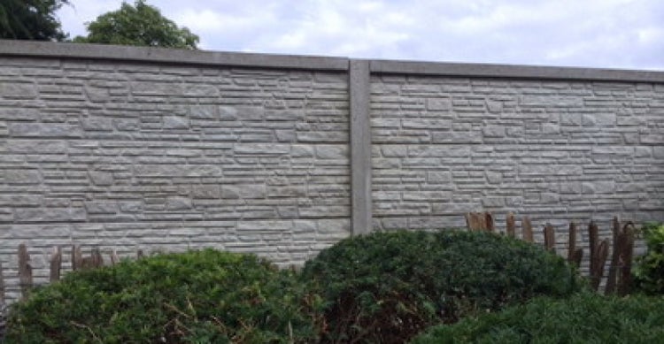 Betonzaun mit Steinmuster und grünen Büschen