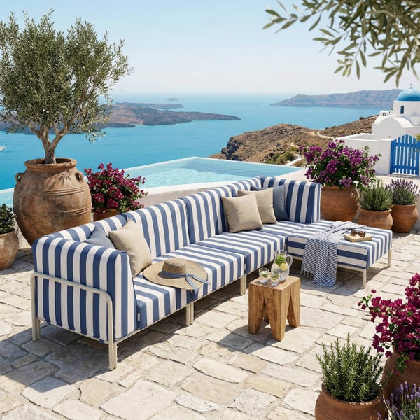 Mediterrane Terrasse mit blau-weiß gestreiftem Outdoor-Loungesofa, Holztisch und Terrakottapflanzgefäßen mit Blick auf das Meer und den Pool.