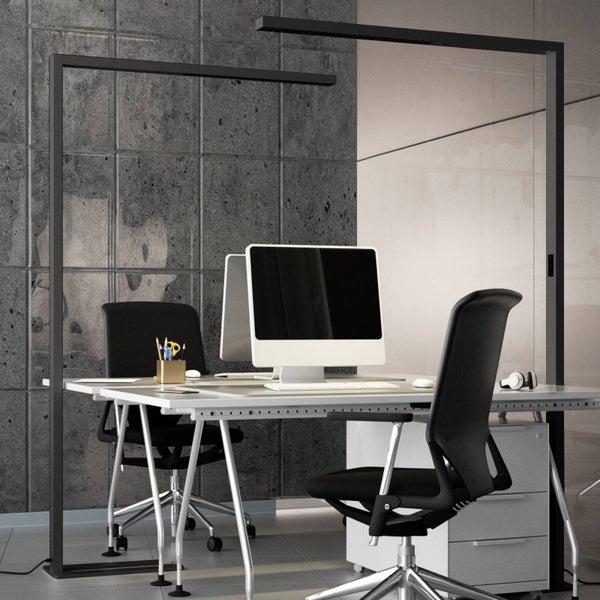 Moderner Büroarbeitsplatz mit zwei Schreibtischen, Bürostühlen und zwei großen Stehleuchten vor einer Wand in Betonoptik.