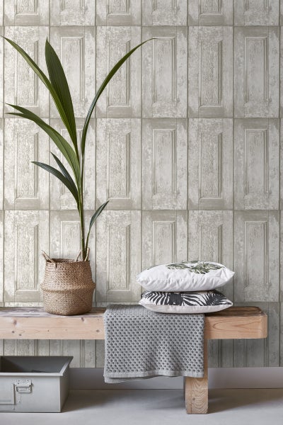 Szene mit einer Zimmerpflanze in einem Korb, Kissen mit Pflanzenmotiven, einer grauen Decke und einer Tapete mit Paneel-Design