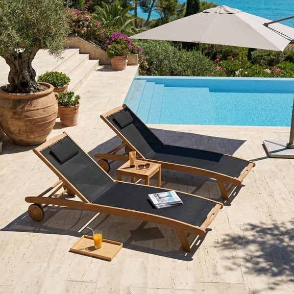 Zwei Gartenliegen aus Holz mit schwarzer Textilbespannung und Kopfstützen an einem Pool, dazwischen ein kleiner Beistelltisch aus Holz.