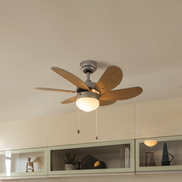 Deckenventilator mit Lampe und sechs Rotorblättern in Holzoptik montiert an einer hellen Zimmerdecke über Wandmöbeln.