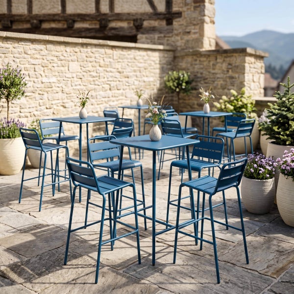 Modernes Gartenmöbel-Set aus blauem Metall auf einer Steinterrasse mit Bistrotischen und Hochstühlen, umgeben von Pflanzen vor einer Steinwand.