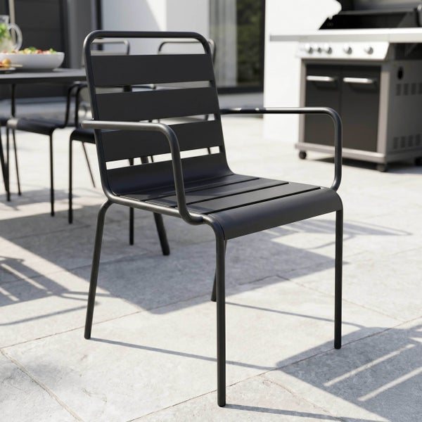 Moderner schwarzer Gartenstuhl aus Metall mit Armlehnen auf einer Steinterrasse mit Grill und Esstisch im Hintergrund.