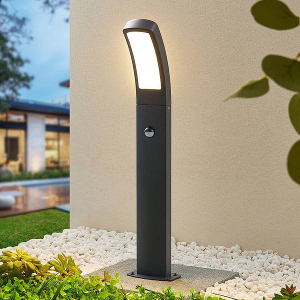 Moderne LED-Wegeleuchte in Anthrazit mit Bewegungsmelder, installiert in einer Gartenanlage mit weißen Kieselsteinen und Pflanzen.