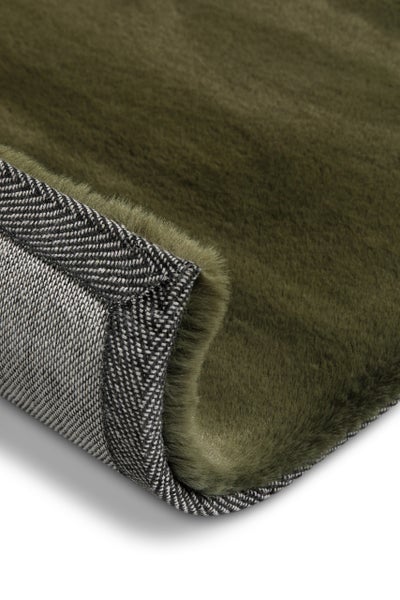 Nahaufnahme eines grünen Kunstfellteppichs mit weicher Textur und gewebter Unterseite mit Fischgrätmuster.