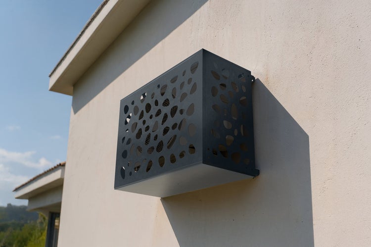 Wandmontierte Klimaanlagenverkleidung mit dekorativen Ausschnitten an einer Hauswand.