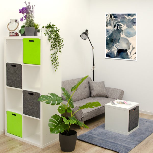 Modernes Wohnzimmer mit weißem Regal, aufklappbarem Sofa, Couchtisch, Zimmerpflanzen und Wandbild in einer hellen und organisierten Einrichtung.
