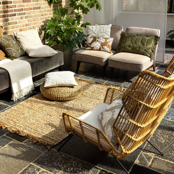 Gemütliche Sitzecke im Freien mit Sofa, Sesseln, Kissen, Teppich und Pflanzen