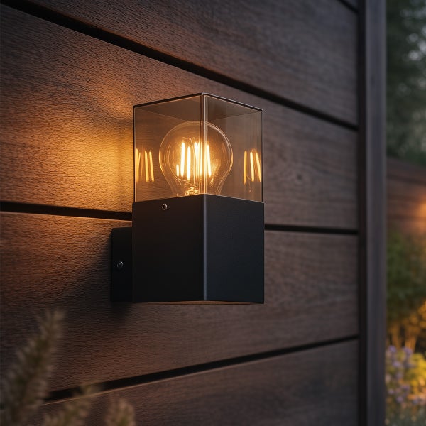 Moderne Außenwandleuchte in Würfelform mit schwarzem Metallsockel und Klarglas, montiert an einer Holzwand mit dekorativem Leuchtmittel.