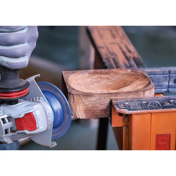 Eine Person benutzt einen Winkelschleifer, um ein Holzstück zu bearbeiten, das in einem Schraubstock fixiert ist.