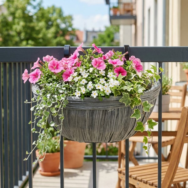 Hängender Balkonblumenkasten in strukturiertem Design, gefüllt mit rosa Petunien und weißen Sommerblumen, montiert an einem Balkongeländer.