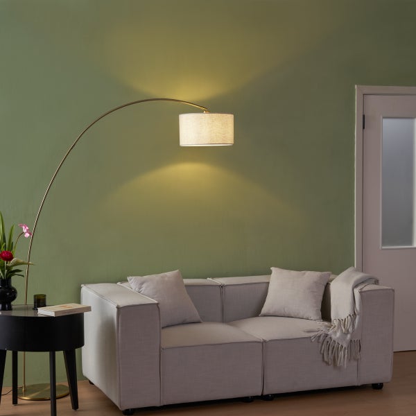 Bogenstehleuchte mit Textilschirm über einer Polstercouch in einem hellen Wohnzimmer.