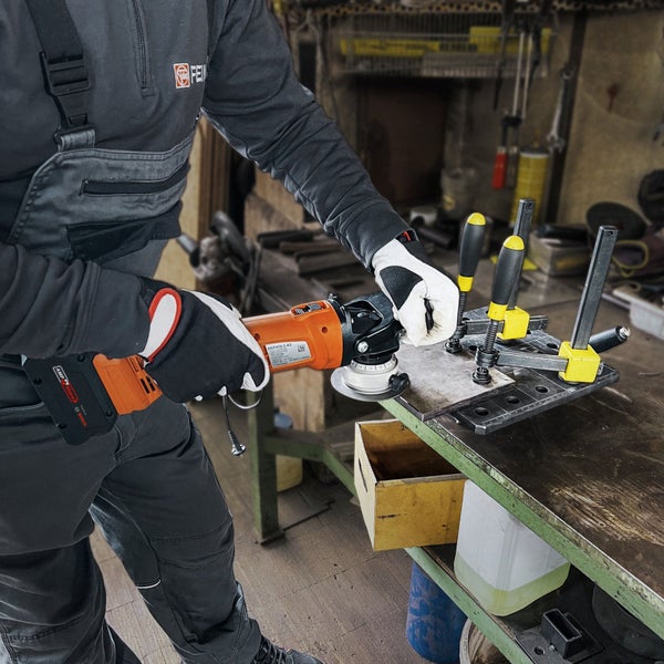 Handwerker bearbeitet eine eingespannte Metallplatte mit einer Akku-Kantenfräse an einer Werkbank in einer Werkstatt.