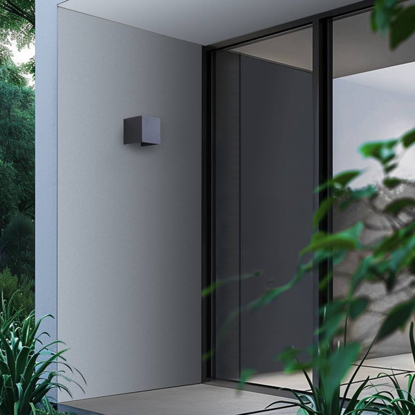 Moderne würfelförmige Außenwandleuchte in Anthrazit an einer grauen Fassade neben einer Glastür im Außenbereich.