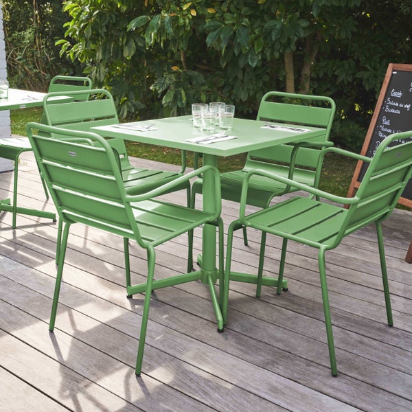 Hell gestaltete Garten-Essgruppe mit quadratischem Metalltisch und passenden Armlehnenstühlen auf einer organisierten Holzterrasse.