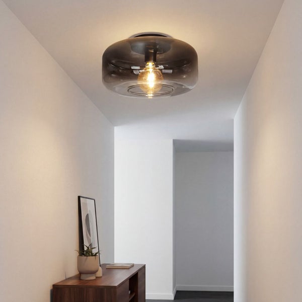 Moderne Deckenleuchte mit Schirm aus Rauchglas in einem hellen Flur über einer Holzkommode.