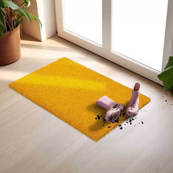 Gelbe Fußmatte vor einer Tür mit schmutzigen Gummistiefeln darauf